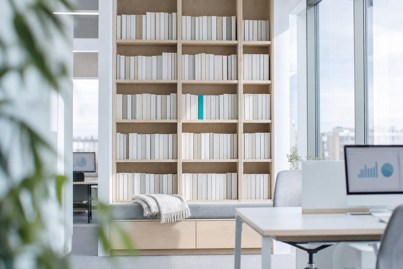 A wall of shelves with white book spines in a light office, one spine in teal